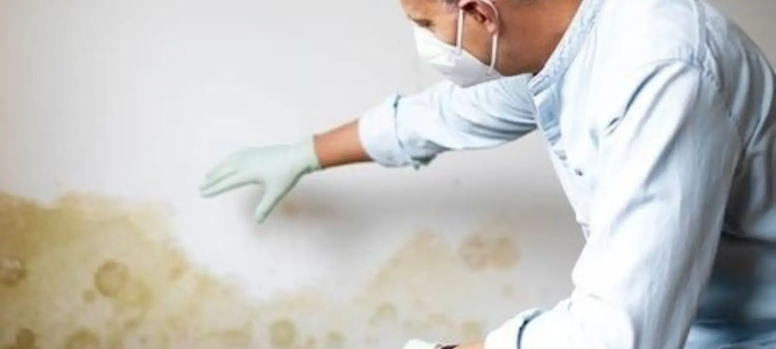 Person in a mask checking a stained wall for water damage
